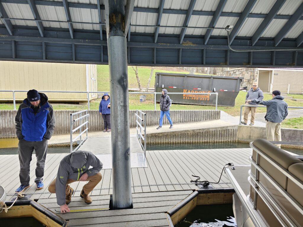 Several people at a boat dock, one of whom is using a tape measure decking.