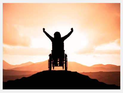A person in a wheelchair at the top of a hill with arms raised