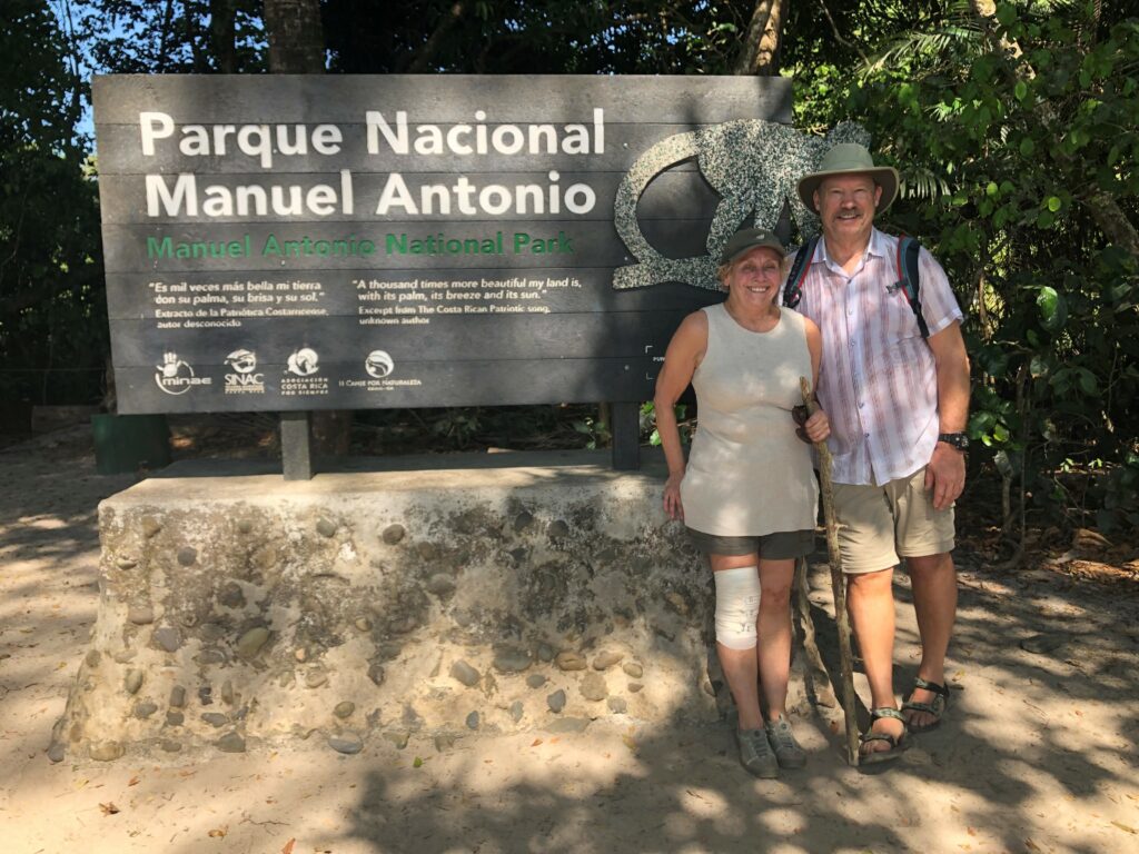 A couple posing next to the entrance sign for Parque Nacional Manuel Antonio