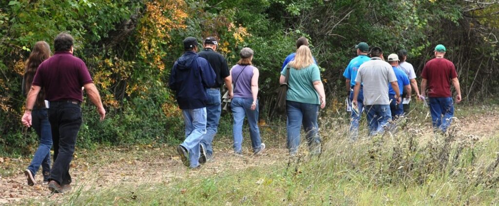 A group of twelve people walking on a grassy trail near trees